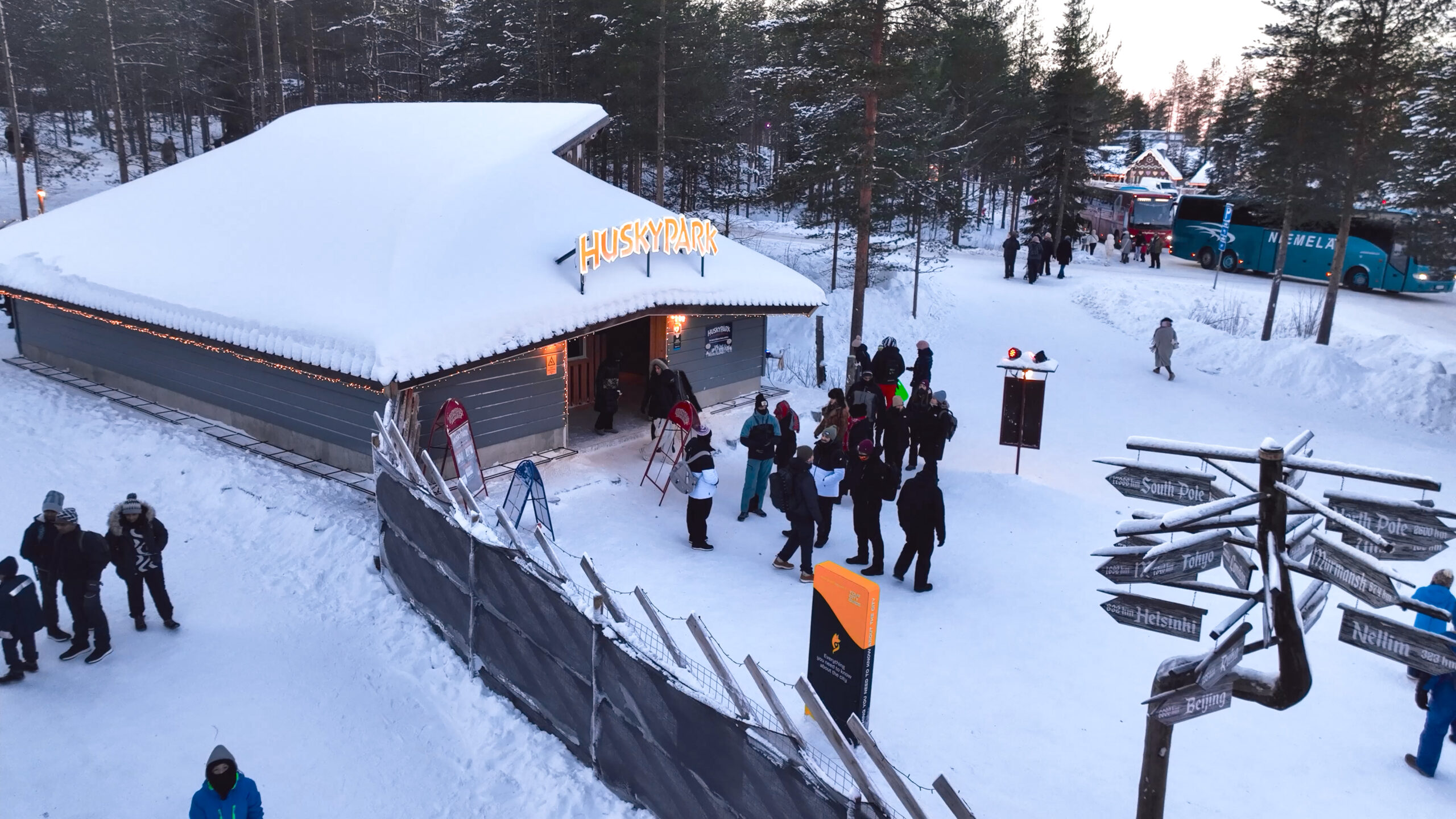 husky park exterior, drone shot high angle. People at the entrance and inside the park, santa claus village in the background